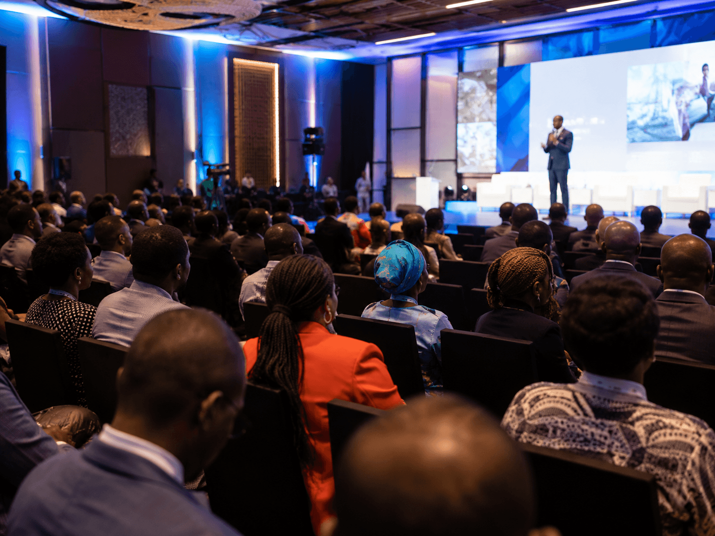 Attendees seated in a conference hall facing a lit stage